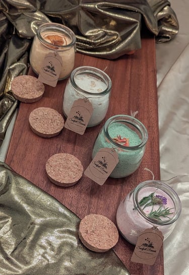 Handmade organic bath salts in glass jars with cork lids and tags on a wooden board.