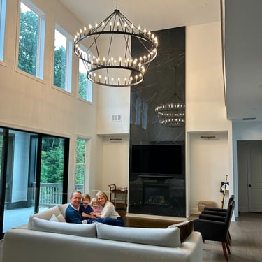 A happy family sits in a modern living room with a large chandelier and black marble fireplace.