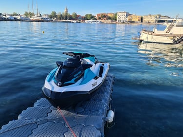A blue and white Sea-Doo jet ski parked on a floating dock in a sunny European harbor.