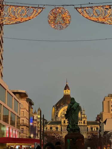 Statue of Peter Paul Rubens in Antwerp facing the illuminated Centraal Station at twilight.
