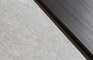 Detail shot of luxury materials: a sample of light grey travertine stone next to a piece of dark charcoal brushed metal. Soft, diffused studio lighting.
