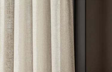 Interior detail: soft light falling on a textured off-white linen curtain next to a dark charcoal window frame.