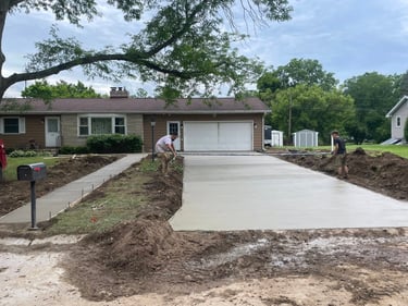 Professional contractors finishing a newly poured concrete driveway and sidewalk for a residential home.