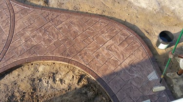 A worker applying a clear sealant to a curved brown stamped concrete walkway with a slate stone pattern.