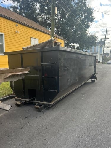 Large black roll-off dumpster rental parked on a residential street for waste removal.
