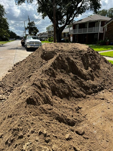Large pile of brown landscaping topsoil delivered on a suburban driveway for ground leveling.