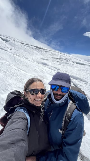 Smiling mountaineers wearing sunglasses and winter gear posing on a snowy mountain glacier slope.