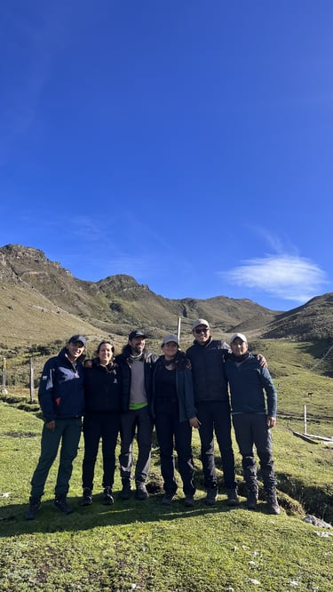 A group of diverse hikers posing together on a grassy mountain trail under a clear blue sky.