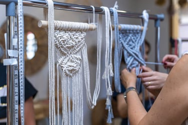 manos tejiendo macrame colgado en un tubo con cinta de medir al lado