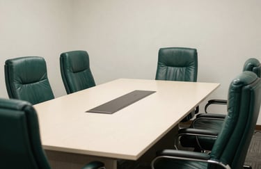 A formal corporate meeting room in a East African / Tanzanian office, with deep forest green leather chairs and an off-white table, conveying a sense of scale and established structure.