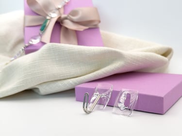 Clear adhesive wall hooks displayed on a purple gift box with white linen fabric.