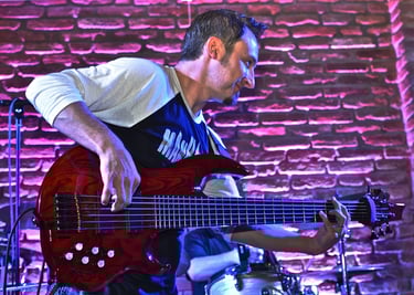 Jozef Bobula on red six-string bass, playing live with a band at a concert event.