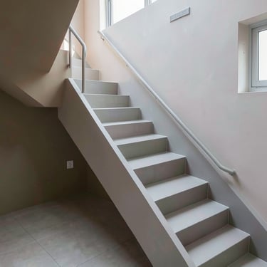 A modern internal staircase finished in light grey microcement with a handrail built into the wall