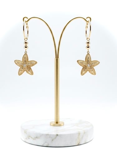 Elegant gold starfish drop earrings featuring a diamond accent on a jewelry display stand.