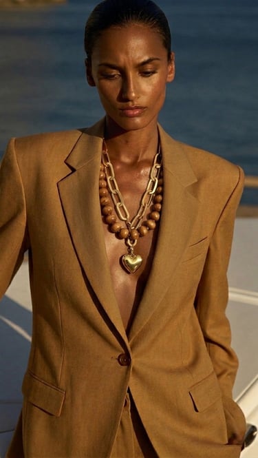 A woman wears a tan linen blazer with chunky gold chain and wood bead heart necklaces.