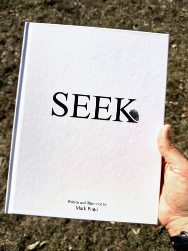 Hand holding hardcover book SEEK with front title visible