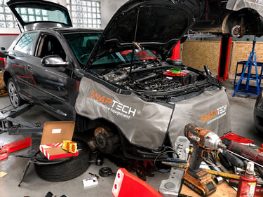 A black car undergoing engine repair and brake service at an auto mechanic shop with professional tools.