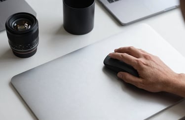 An overhead shot of a person using a high-precision mouse on a clean, soft silver desk pad. Minimalist office supplies in charcoal black are arranged neatly.