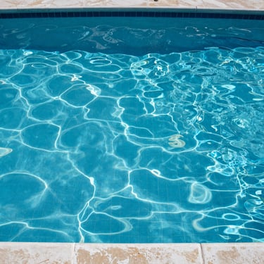 A high-quality photo of a residential pool with crystal blue water, showing clean tile lines and a well-maintained surface in South Florida.