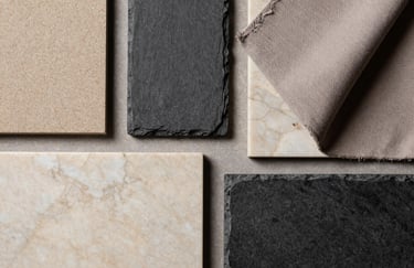 A flat lay photography of high-end material samples including soft sand marble, charcoal slate, and taupe fabrics in a Southern European / Spanish (Madrid) design studio.