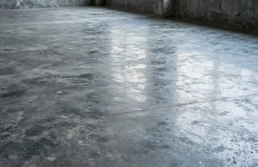A close-up of a high-quality finished concrete floor in a modern South American / Brazilian building. The surface is smooth and reflects silver-grey and dark charcoal blue tones from the industrial interior.