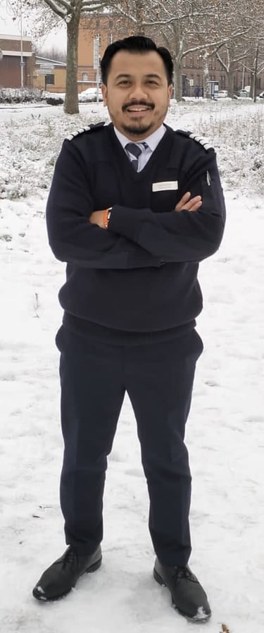 Asian Hotel Manager in a dark blue uniform standing with crossed arms in a snowy outdoor field.