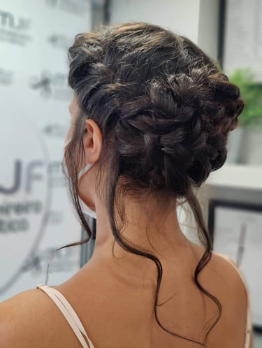 Elegant braided low bun bridal updo on brunette hair with loose wavy tendrils for a wedding hairstyle.