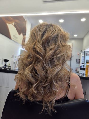  long honey blonde hair with voluminous curls and balayage highlights in a hair salon.