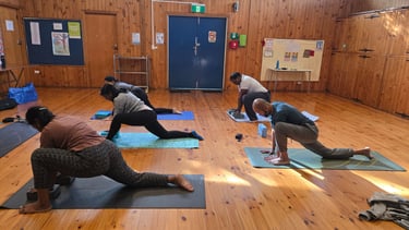 Diverse group practicing low lunge yoga poses on mats in a rustic wooden studio with blocks.
