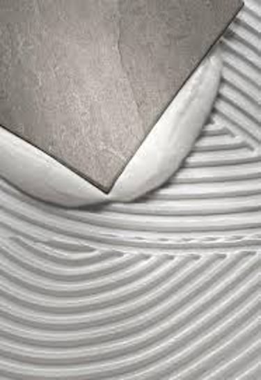 A ceramic tile being pressed into white thin-set mortar adhesive for flooring installation.