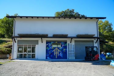 Industrial warehouse with colorful abstract mural and a red forklift parked in front of rolling doors.