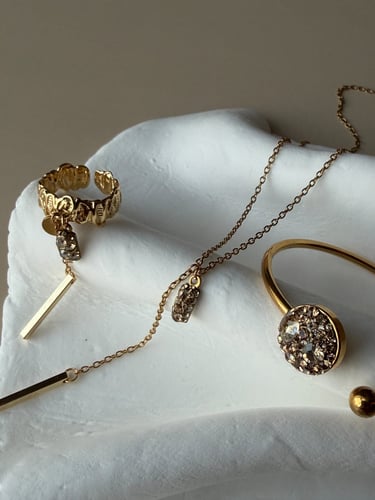 Elegant gold jewelry set with crystal charms including a ring, necklace, and bangle on a white ceramic surface.