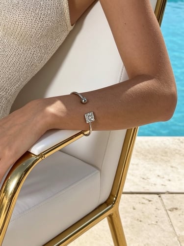 A woman's arm wearing a silver open cuff bracelet with a diamond square charm by a luxury swimming pool.