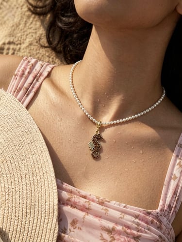 A white pearl necklace with a gold seahorse pendant worn by a woman on a sunny beach.
