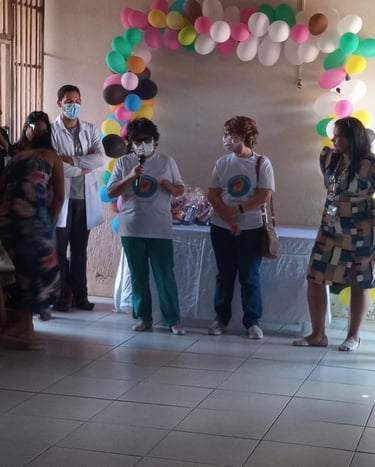 Healthcare workers wearing masks speak at a community event with colorful balloon decorations.