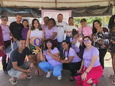 A group of people gathering around a pregnant woman with a baby painting on her belly for a maternity event.