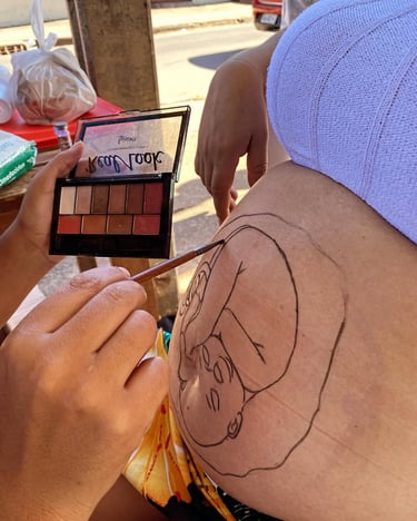 Artist uses a makeup palette to paint a detailed baby outline on a pregnant woman's belly.