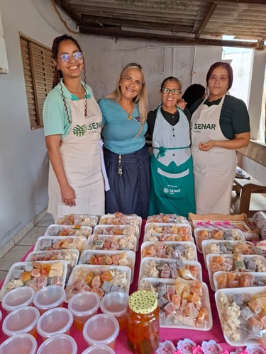 Four women smiling behind a table filled with trays of homemade fruit preserves and sweets from SENAR Goiás.