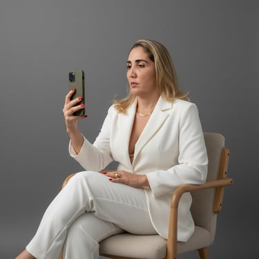 Professional woman in a white power suit sitting in a chair and looking at her smartphone.