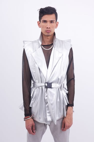 Male model wearing a futuristic metallic silver vest over a black mesh shirt for avant-garde fashion.