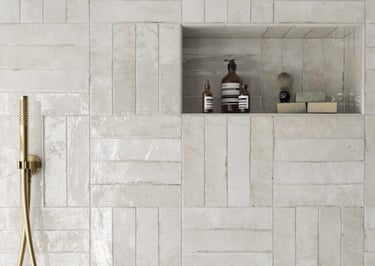 White gloss subway tile shower wall with gold hardware and built-in storage niche.