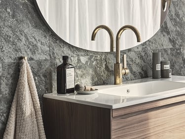 Modern bathroom vanity with a gold faucet, white sink, and grey marble tile backsplash.
