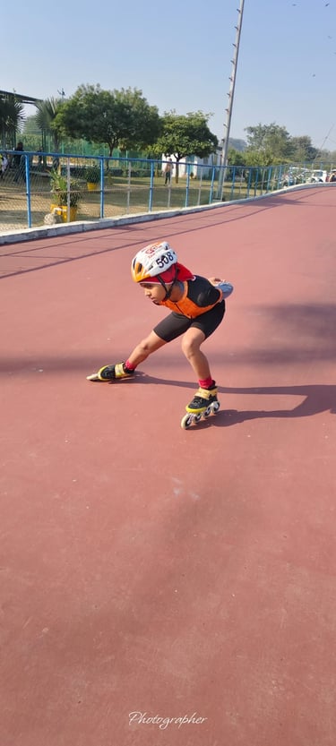 A young speed skater in a helmet and racing suit practices on an outdoor roller skating track.