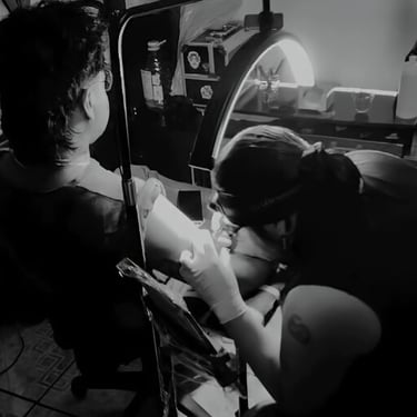 Tatuador profesional aplicando tinta en el brazo de un cliente bajo una iluminación brillante.