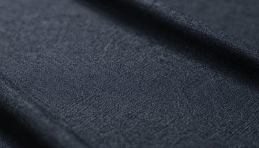 A professional apparel designer's workstation with digital patterns on a large screen and fabric swatches in various shades of #4A5568.