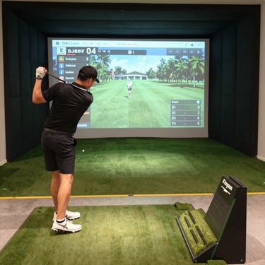 A cozy golf simulator bay with a vibrant sports bar visible in the background.