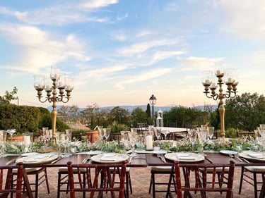 Elegant outdoor wedding reception table setting with gold candelabras and sunset views.