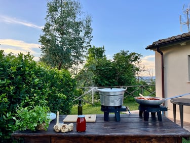 Outdoor cooking setup with large pots on gas burners, fresh herbs, and garlic on a wooden table.