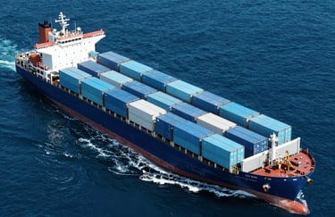 Top-down view of a massive cargo ship slicing through deep blue ocean water (#0A1F2C), with light blue shipping containers arranged with geometric precision. High-contrast, sleek aesthetic.
