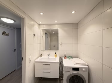 Modern white tiled bathroom featuring a floating vanity sink, large mirror, and a front-load washing machine.